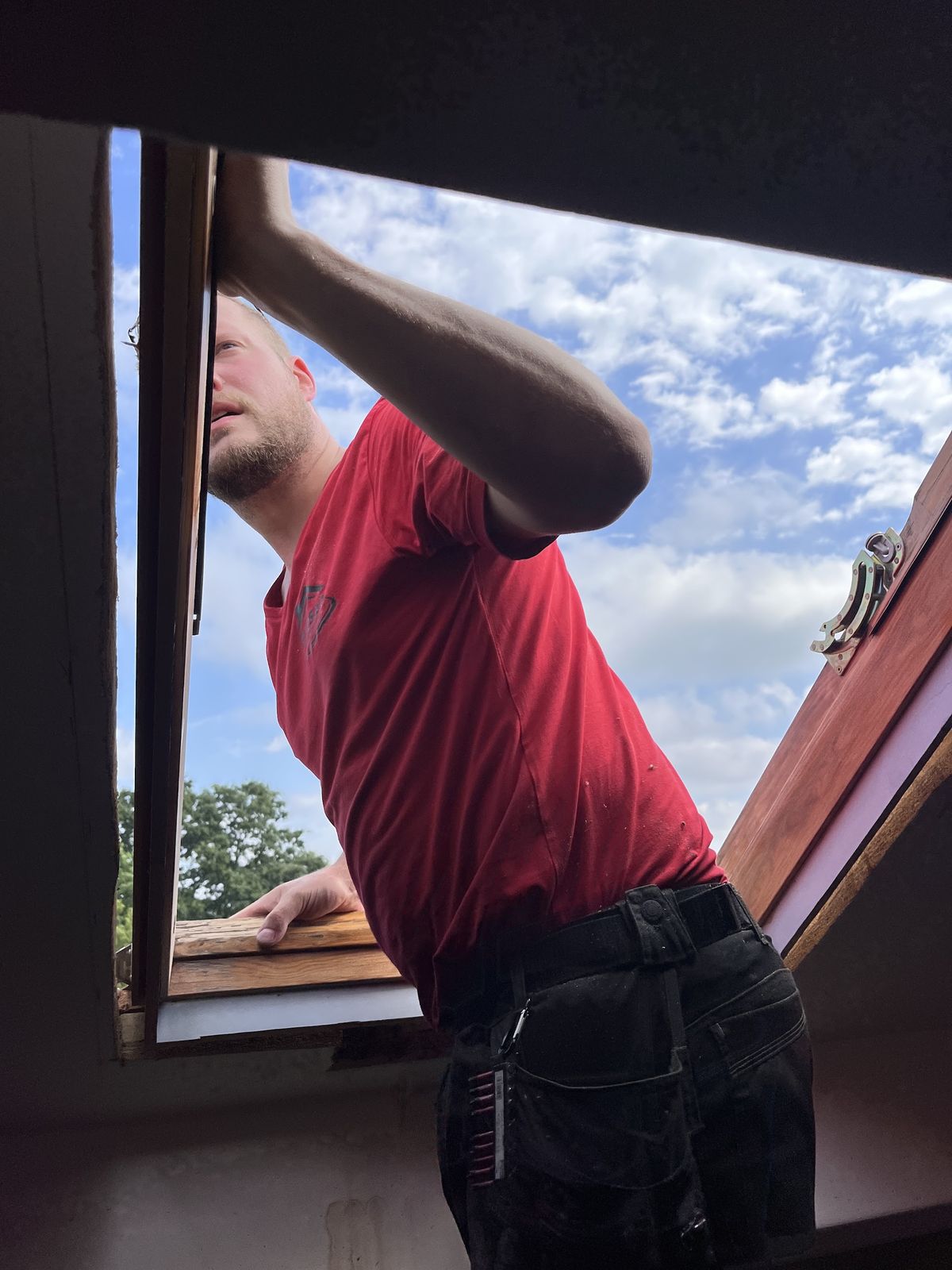 Vakman plaatst een nieuw dakraam, van binnenuit gezien met blauwe lucht erachter