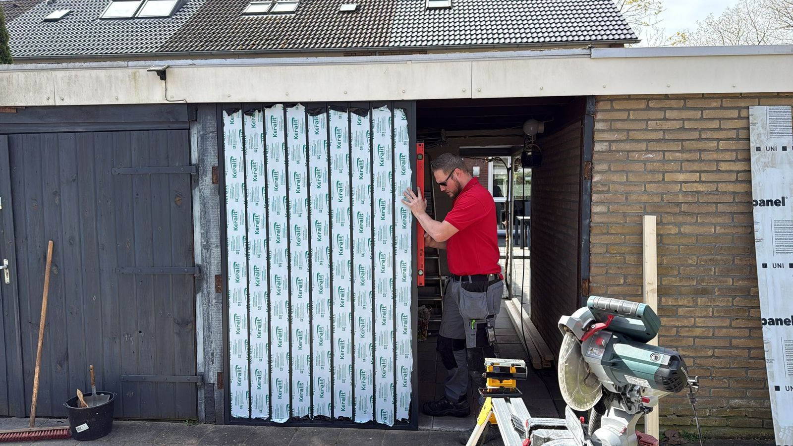 Vakman in rood shirt stelt met een waterpas een nieuw paneel in beschermfolie af in de opening van een garage