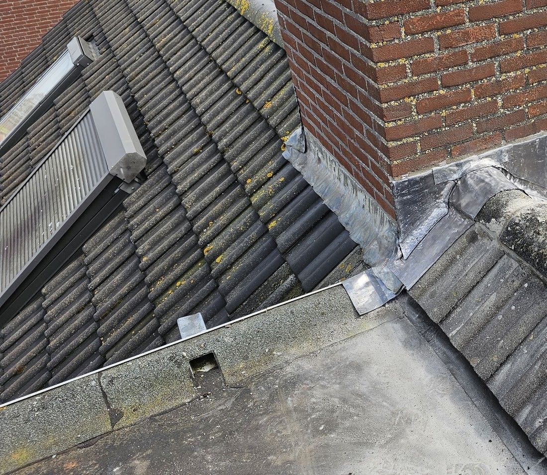 Loodwerk rond een bakstenen schoorsteen op een pannendak, bij een plat dak