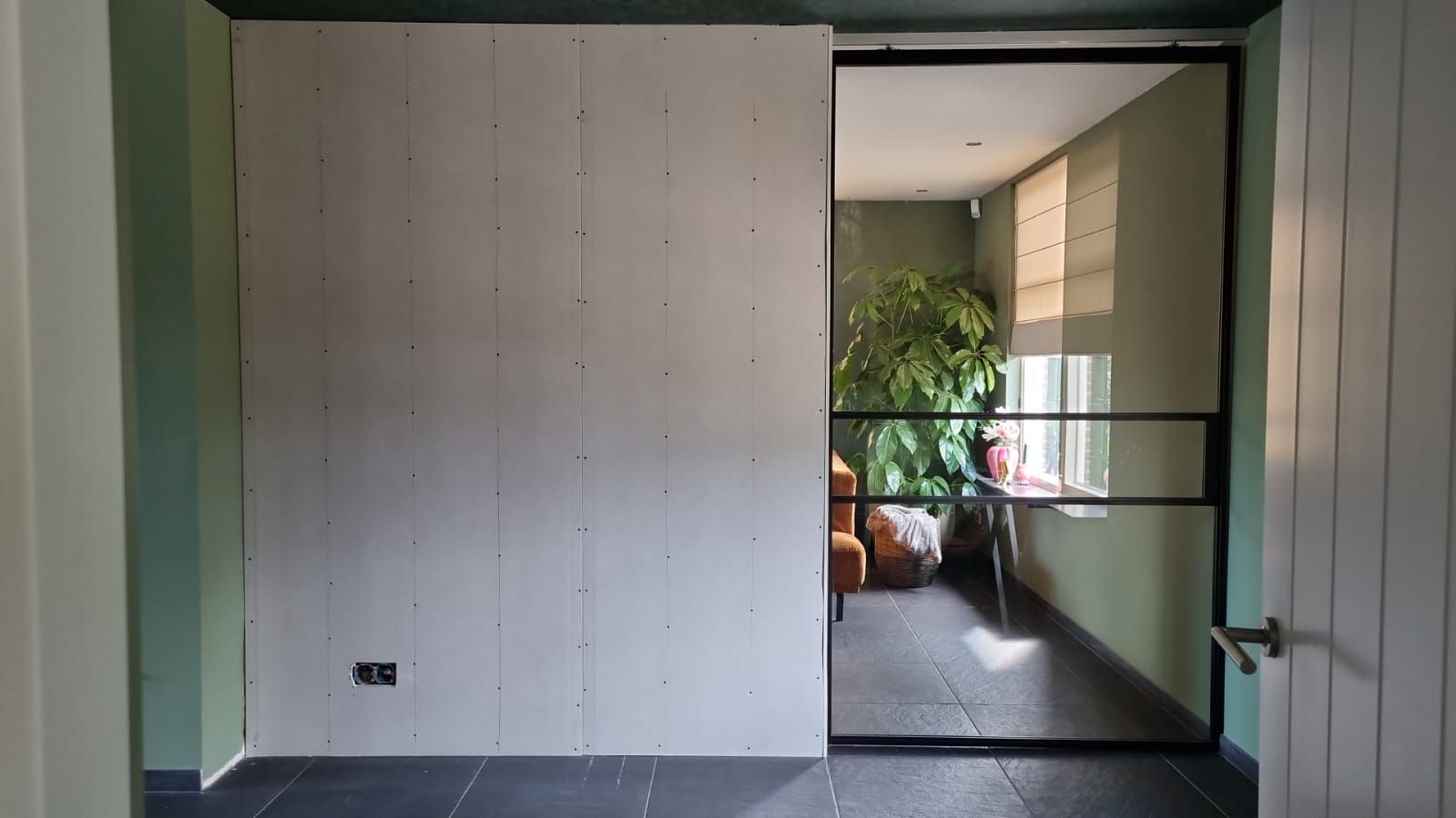 Nieuwe binnenwand van geschroefde platen naast een stalen glazen schuifdeur